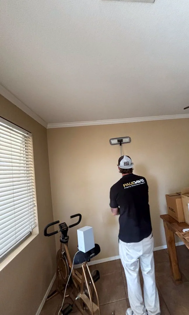 A Paul Davis crew member cleaning a room wall with a long-handled tool.